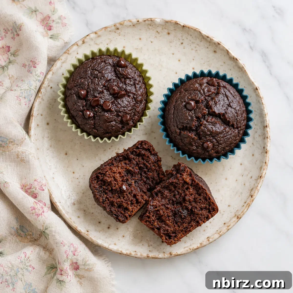 three vegan chocolate buckwheat muffins on a stoneware plate, with one cut open